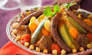 Un plat généreux de couscous royal, garni de merguez, de morceaux de viande, de légumes et de pois chiches, prêt à être dégusté.