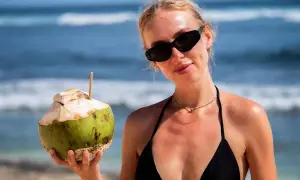 Kobieta w czarnym bikini trzyma kokosa na plaży. Idealne wakacje na Bali!