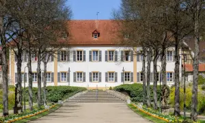 Prachtvolles Gebäude in Bad Bocklet, ideal für Ayurveda-Anwendungen. Ein Weg führt durch einen Garten mit Statuen und Blumen zum Eingang.
