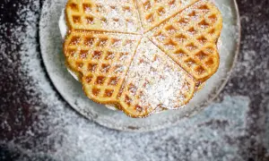Herzförmige Waffeln, bestäubt mit Puderzucker, warten auf ein köstliches Waffeln Rezept.