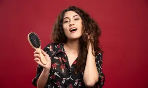 Ragazza con capelli ricci pettinati, tiene in mano una spazzola per capelli.