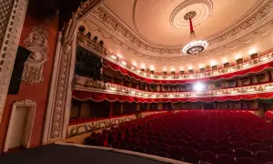 Wnętrze teatru z czerwonymi fotelami i bogato zdobionymi lożami. Czekamy na rozpoczęcie spektaklu, by usłyszeć piękną **arię**.