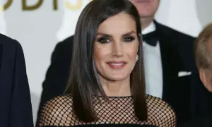Elegancka królowa Letizia w czarnej, siateczkowej kreacji, z błyszczącymi oczami i uśmiechem, pozuje do zdjęcia z innymi osobami.