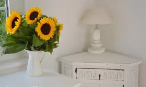 Strahlende sonnenblumen in der vase bringen Sommerstimmung in die Ecke, neben einer weißen Lampe auf einem antiken Schränkchen.