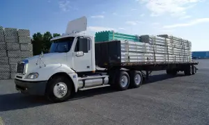 Camion blanc prêt pour le transport, avec un chargement de tuyaux blancs et verts bien sécurisé. L'arrimage des charges est essentiel pour un trajet sûr.