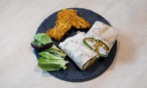 Pyszny kebab w tortilli, idealnie zawinięty, z chrupiącymi kawałkami kurczaka i świeżą sałatką.