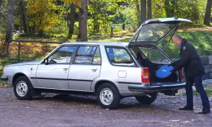 Man lastar en blå frisbee i bakluckan på en silverfärgad Renault 18 kombi i höstlandskap.