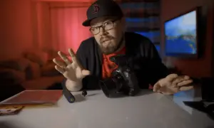 Mężczyzna w czapce z daszkiem i okularach opowiada o sprzęcie do vlogu. Na stole leży aparat, uchwyt i akcesoria.