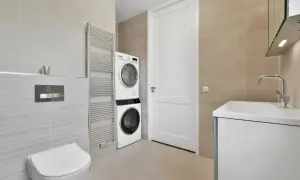 Bagno moderno con lavatrice e asciugatrice impilate, un termoarredo, un WC e un lavabo. Soluzione salvaspazio per nascondere lavatrice in bagno.