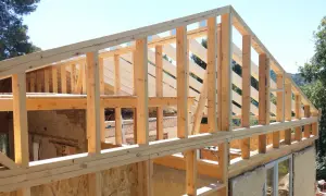 Estructura de madera para casa en construcción, con vigas y pilares de madera a la vista bajo un cielo azul.