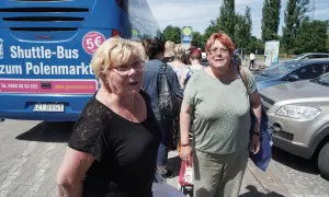 Zwei Frauen warten auf den Shuttle-Bus zum Polenmarkt. Der blaue Bus wirbt mit "5€ Fahrpreis".