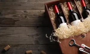 Drewniana skrzynka z trzema butelkami marani wino półsłodkie, wypełniona słomą. Obok korkociąg i korki.