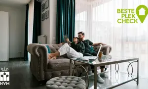 Een stel overweegt wel of niet verhuizen, zittend op de bank met een laptop. De "Beste Plek Check" logo suggereert hulp bij deze beslissing.