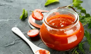 Un pot de ketchup maison, garni de fraises et de feuilles vertes, sur fond sombre.