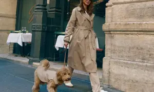Elegancka kobieta w beżowym płaszczu, idealnym przykładzie, jak nosić płaszcz damski, spaceruje z psem po ulicy.