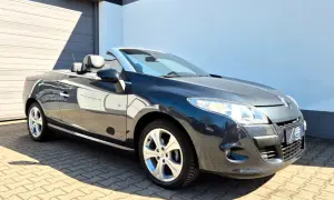Ciemnoszary Renault cabrio z opuszczonym dachem, zaparkowany na wybrukowanym podjeździe przed budynkiem.