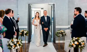 Panna młoda w sukni ślubnej idzie z ojcem do ołtarza, trzymając bukiet.