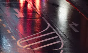 Nasse Straße mit roten und weißen Lichtreflexionen. Pfeile auf dem Asphalt zeigen die Fahrtrichtung an, wie bei einer anhalteweg formel.