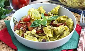 Tortellini z pesto, pomidorkami koktajlowymi i bazylią w białej misce.