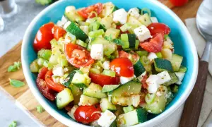 Frischer Zucchini Salat mit Tomaten, Feta und Frühlingszwiebeln in einer blauen Schüssel. Ein leichter Genuss!