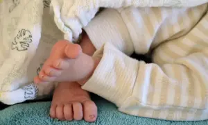 Stópki dziecka w paski, otulone kocykiem z motywem liści. Delikatne paluszki, jakby walczyły z chorobą pandas.