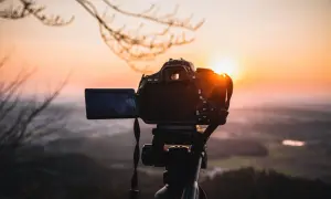 Aparat fotograficzny na statywie na tle zachodzącego słońca.