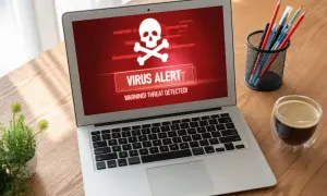 Laptop z czerwonym ekranem i ostrzeżeniem "VIRUS ALERT". To pokazuje, co robi trojan: infekuje system i wyświetla alarm.