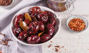 Schwarze, glänzende, fermentierte Pflaumen in einer Schüssel, bereit zum Genießen. Gewürze wie Nelken und Chiliflocken deuten darauf hin, wie man fermentierte Pflaumen selber machen kann.