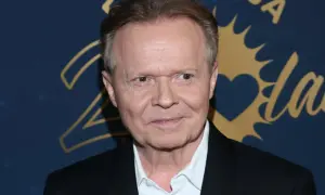 Michał Bajor w czarnym garniturze i białej koszuli, z uśmiechem na twarzy. Choć nie widać jego żony, jego spojrzenie zdaje się mówić o szczęściu.