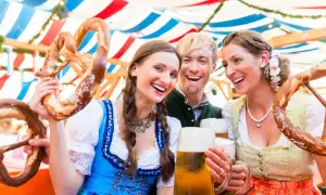 Tre amici sorridono felici sotto i tendoni dell'Oktoberfest, con brezel giganti e boccali di birra.