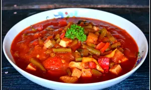 Pyszne leczo z tofu, z fasolką szparagową i papryką w sosie pomidorowym, udekorowane natką pietruszki.