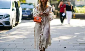 Kobieta w sukience boho z haftem i pomarańczową torebką. Idealne buty do sukienki boho to delikatne sandałki na obcasie.