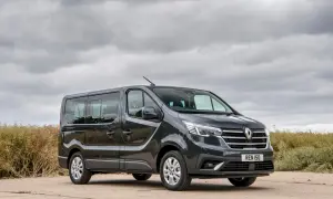 Ciemnoszary Renault Trafic, najmniej awaryjny van 7-osobowy, stoi na tle pochmurnego nieba i zarośli.