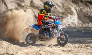 Dziecko w stroju motocyklowym na motocyklu crossowym, wzbijające tumany piasku.