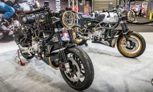 Dwa stylowe motocykle dwusuwowe, jeden czarny z elementami złota, drugi srebrny, prezentowane na wystawie.