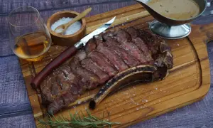 Ein saftiges Cote de Boeuf, perfekt geschnitten, mit grobem Salz bestreut, daneben ein Glas Whiskey, ein Messer und eine Sauce.