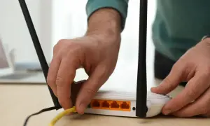 Ręka podłącza żółty kabel do routera. Dowiedz się, jak wzmocnić sygnał wifi domowym sposobem, by cieszyć się lepszym zasięgiem.