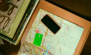 Zielona karta płatnicza, telefon i mapa leżą obok książek. Może to być przygotowanie do podróży, gdzie przyda się waluta Rumunii.