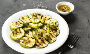 Zucchine alla scapece non fritte, grigliate e condite con olio e spezie, servite su un piatto bianco con una ciotolina di condimento.