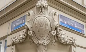 Bogaty herb zdobi fasadę kamienicy, obok tabliczek z nazwami ulic "Za Bramką" i "Wszystkich Świętych".