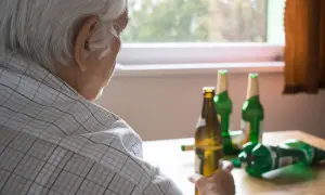 Starszy mężczyzna zmagający się z alkoholizmem, siedzi przy stole z kilkoma pustymi butelkami po piwie.