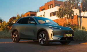 Nowy Geely EX5 w kolorze zielonym, zaparkowany przed nowoczesnymi domami.