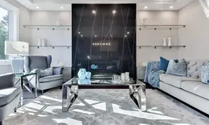 Elegancki salon z kominkiem obłożonym czarnym marmurem i **ścianami w stylu glamour**. Szare fotele, sofa i szklane półki tworzą luksusową atmosferę.