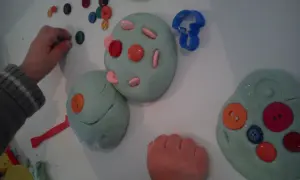 Manos infantiles jugando con plastilina casera, decorada con botones de colores y cortadores.
