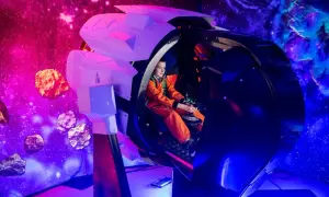 Chłopiec w pomarańczowym kombinezonie steruje statkiem kosmicznym w symulatorze. Kosmopark Wrocław oferuje kosmiczne przygody wśród asteroid i mgławic.