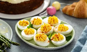 Une assiette d'œufs mimosa, une entrée traditionnelle de Pâques, avec un gâteau aux carottes et des œufs décorés en arrière-plan.
