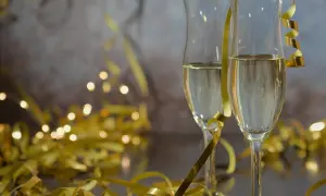 Dwa kieliszki szampana, złote serpentyny i migoczące światełka tworzą atmosferę noworocznych przesądów i celebracji.