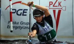 Młody mistrz polski w kajakarstwie, w kasku i kamizelce z numerem 11, wiosłuje w wodzie.