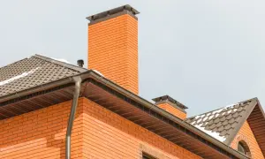 Eleganckie zakończenie komina systemowego z cegły, zwieńczone metalową nakładką, chroni przed warunkami atmosferycznymi.