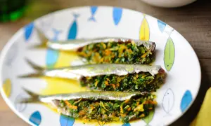 Trois sardines farcies aux herbes et légumes, servies sur une assiette décorée de poissons.